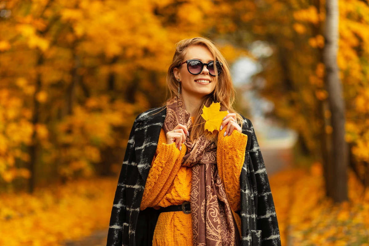 fall-lighting-conditions a woman standing outside during fall smiling and holding a leaf