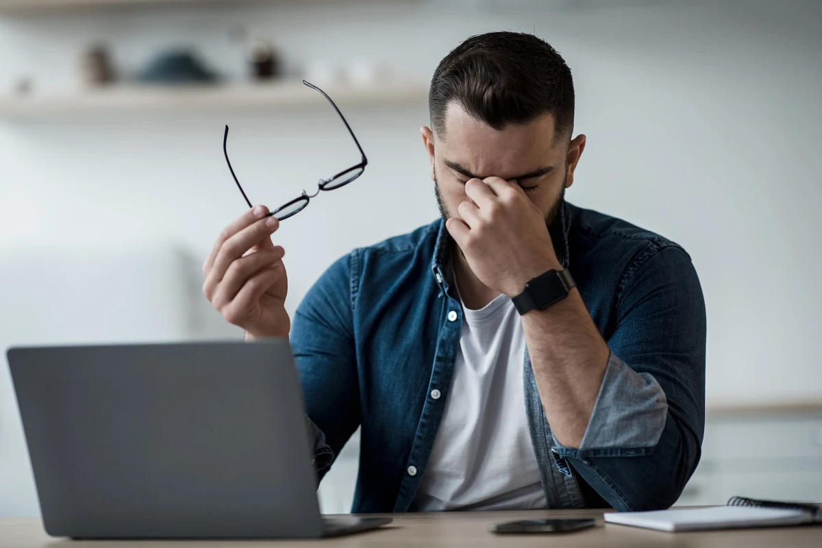 a man taking off his glasses and putting a hand to his face while working