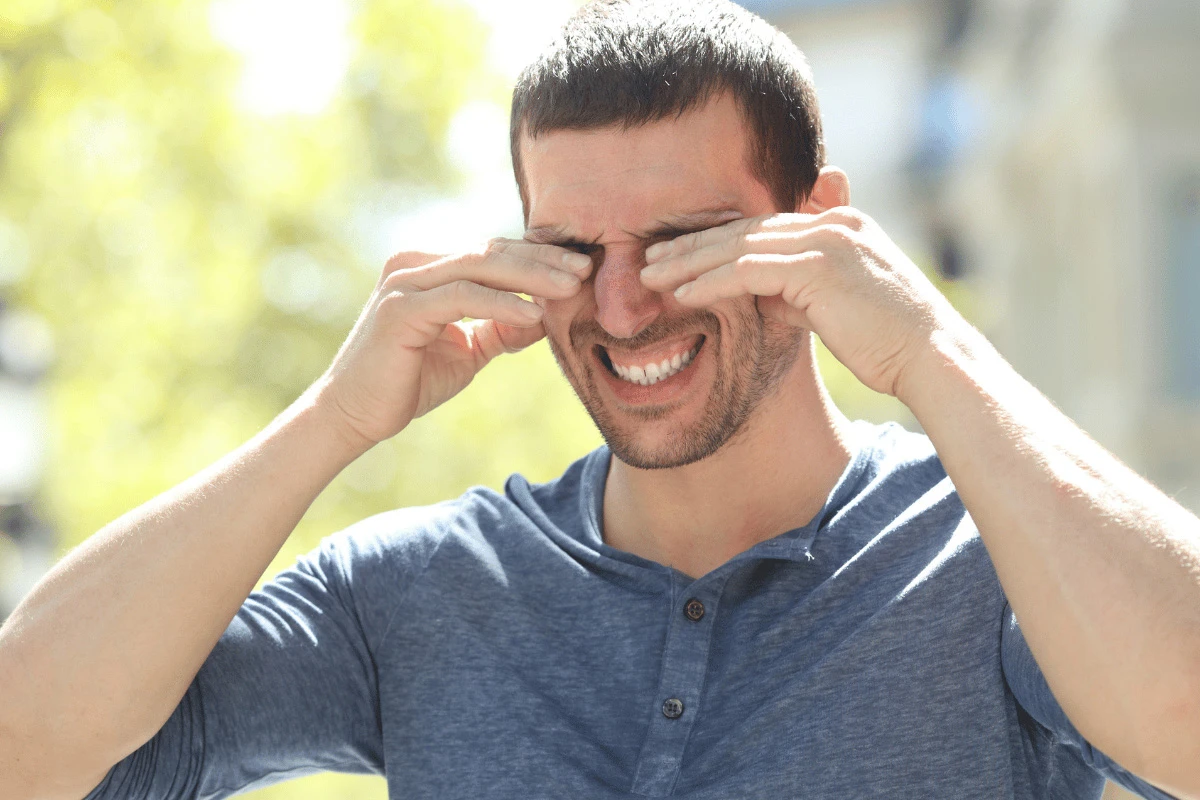 a man standing outdoors rubbing his eyes