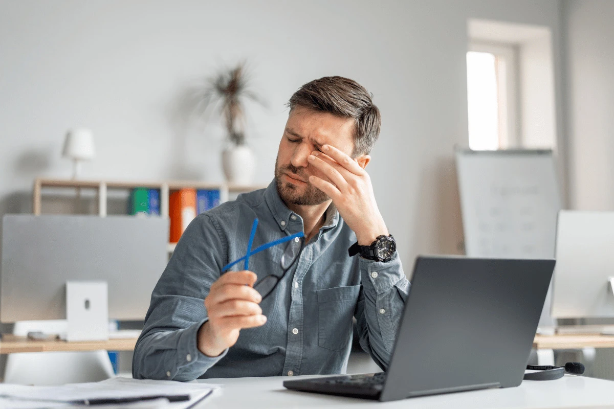 a man sitting in front of his computer and rubbing his irritated eyes