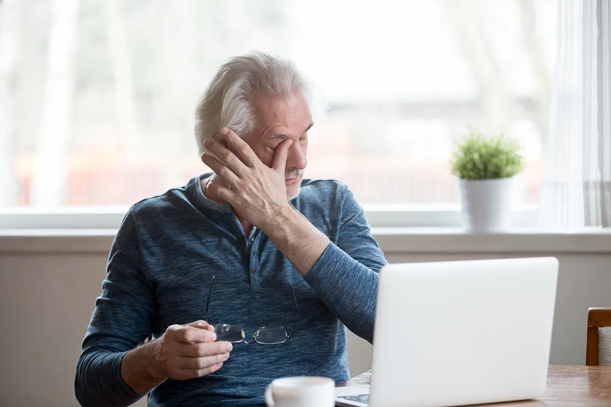 an older man taking off his glasses and rubbing his irritated, dry eye
