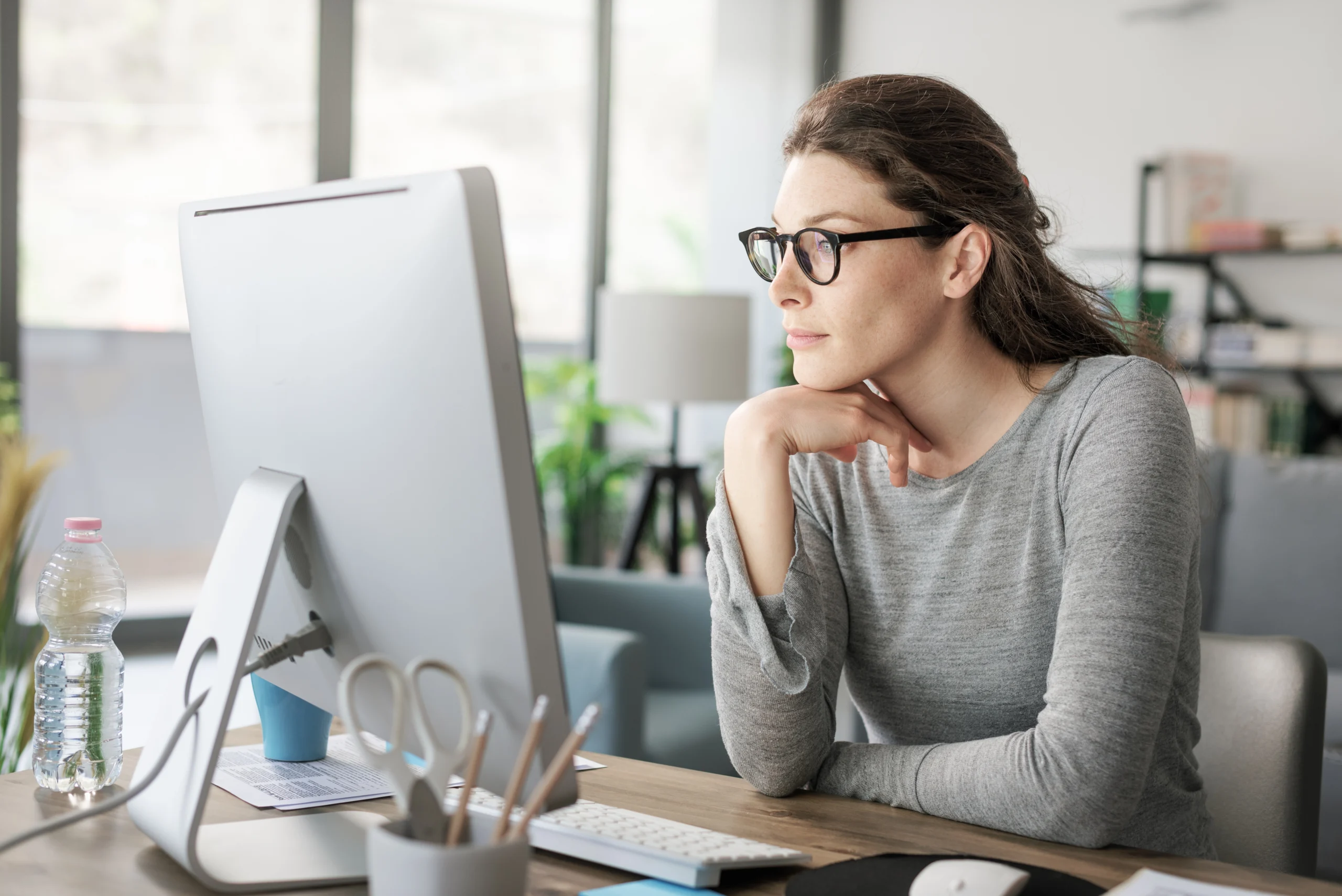A woman wearing glasses leans forward to look at her computer.