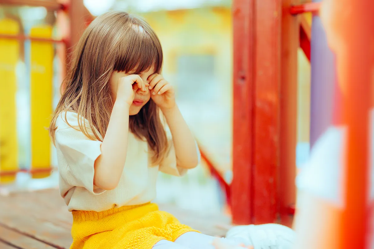 a little girl rubbing her eye outside at the playground