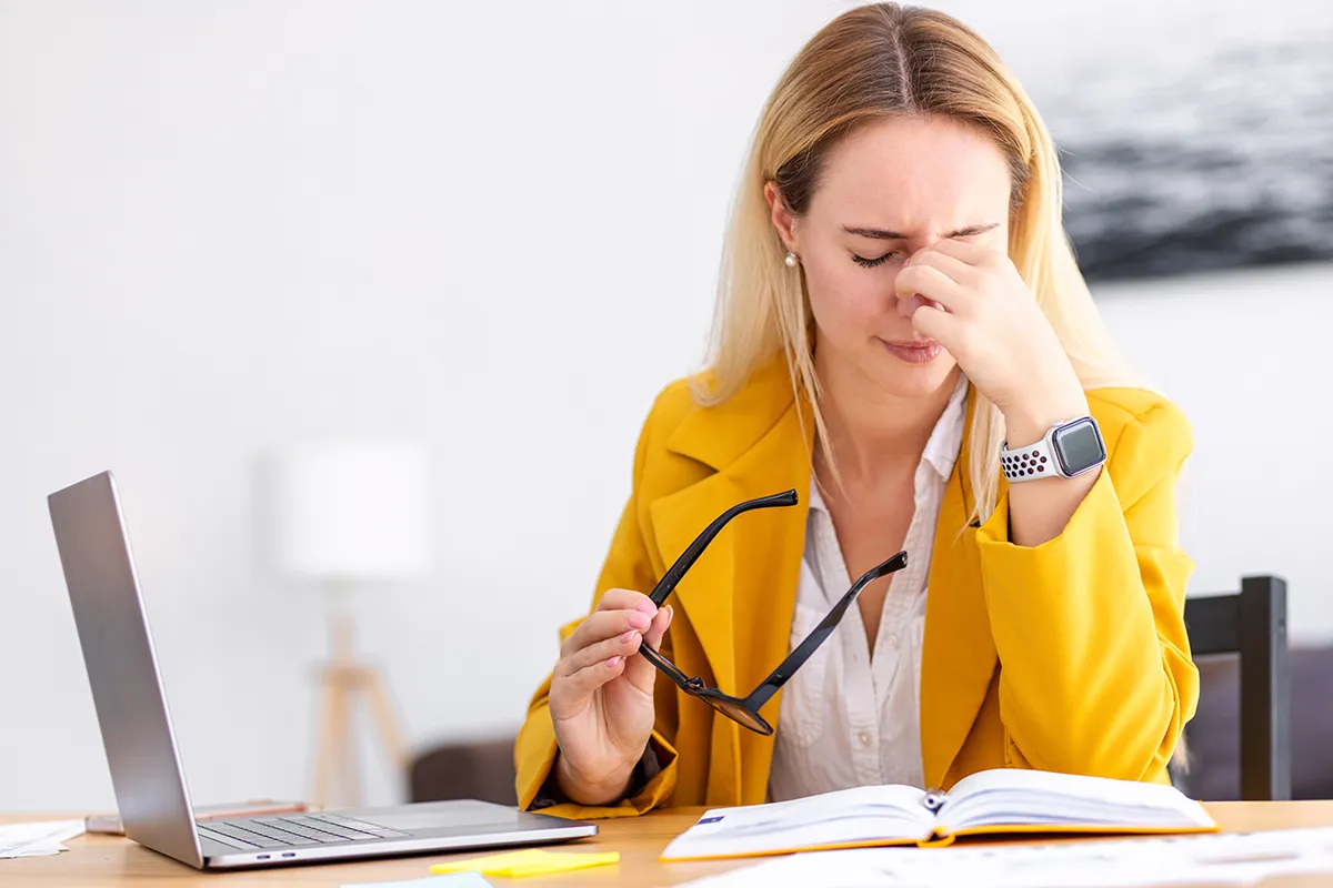 a young woman taking off her glasses at work and looking uncomfortable